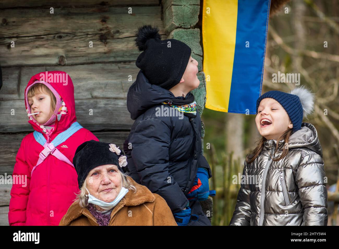 Beautiful Ukrainian children or kids with grandmother near a wooden house with flag of Ukraine during the invasion of Russia, war refugees Stock Photo