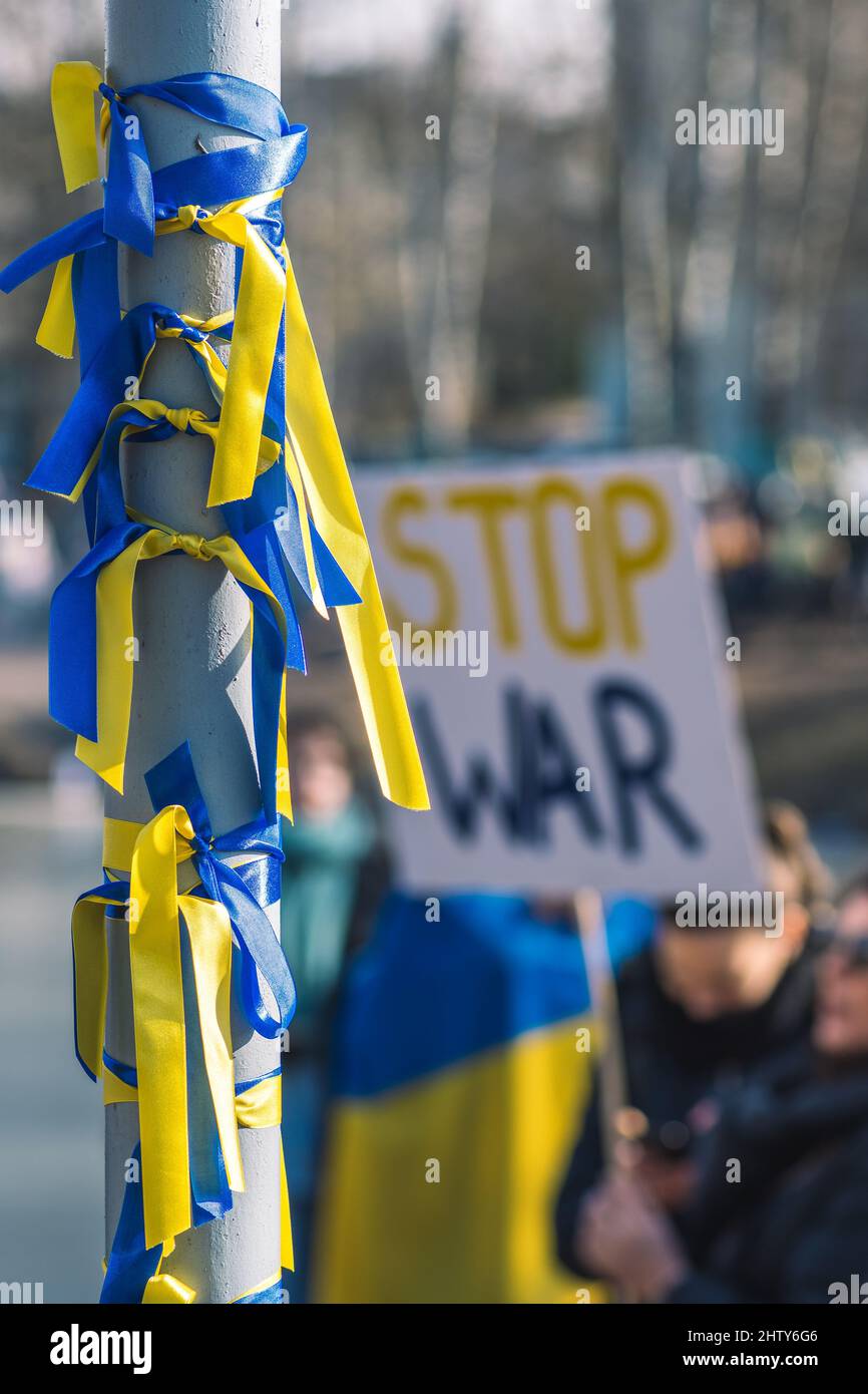 Ribbons with colors of Ukraine during a peaceful demonstration against war, Putin and Russia, Ukrainian and Stop War placard on background, vertical Stock Photo