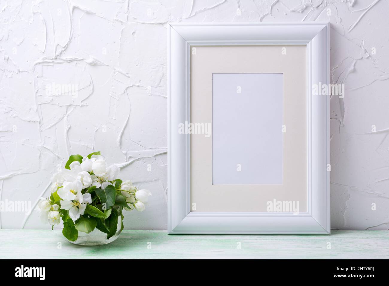 White frame mockup with apple blossom in the small glass vase. Empty frame mock up for presentation artwork. Template framing for modern art. Stock Photo