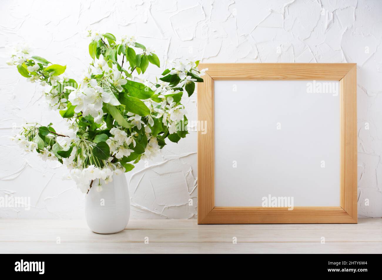 Wooden square picture frame mockup with tender apple blossom branches in the vase. Empty frame mock up for presentation design. Template framing for m Stock Photo