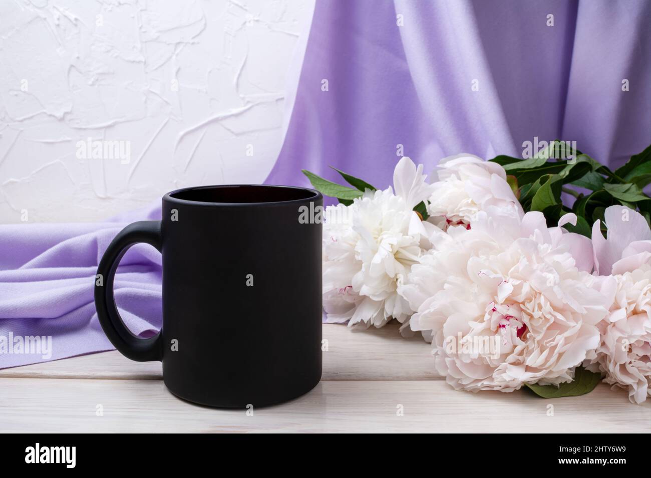 Black coffee mug mockup with pale pink peony and lilac scarf. Empty mug mock up for brand promotion Stock Photo