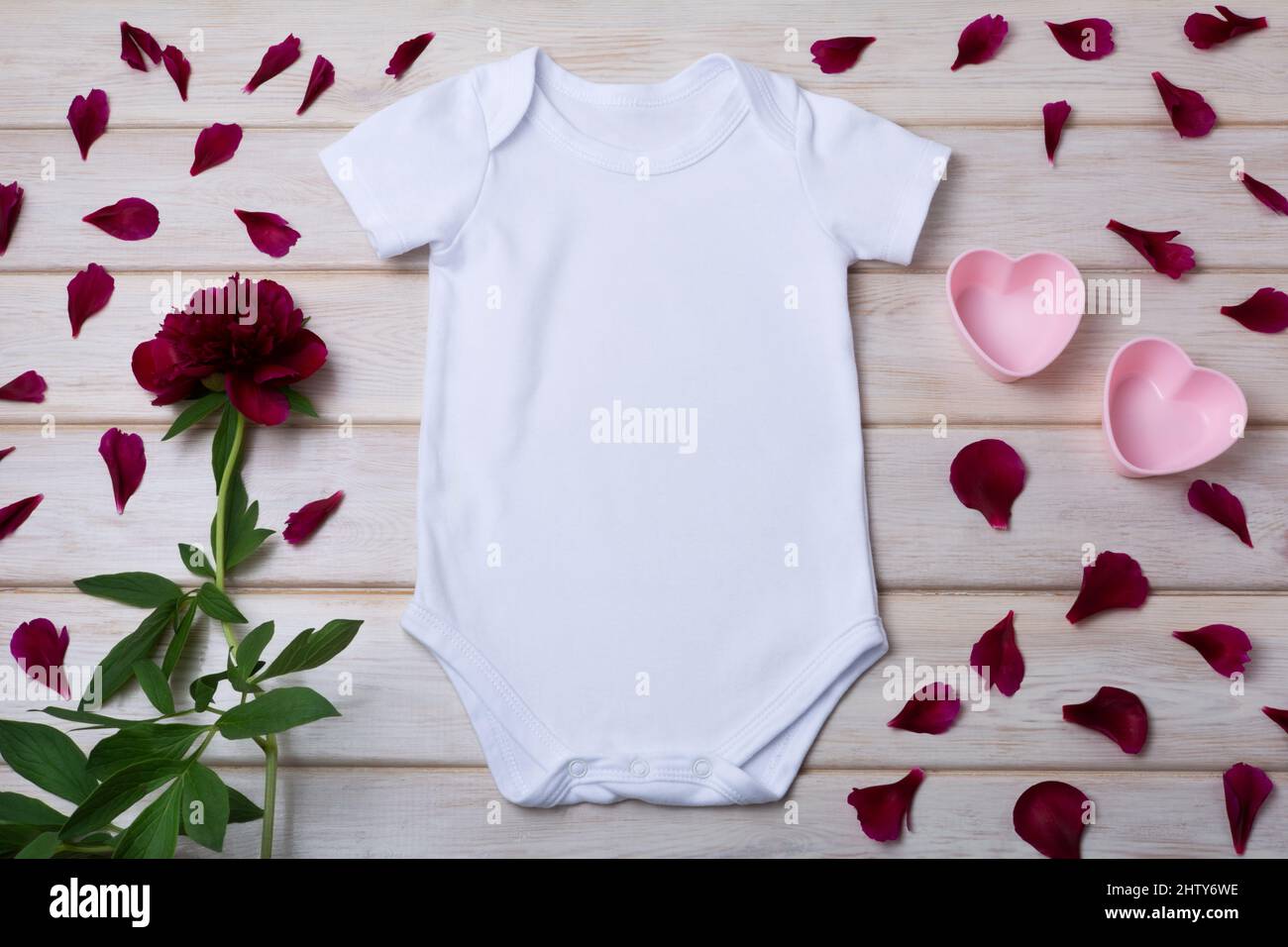 White cotton baby short sleeve onesie mockup with two pink hearts, maroon peony and petals. Design gender neutral bodysuit template, newborn romper pr Stock Photo