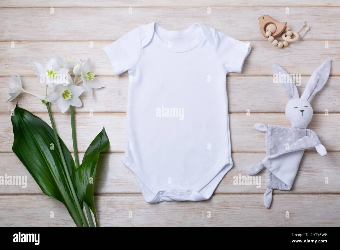 White cotton baby short sleeve onesie mockup with tender lily bouquet, wooden bird toy and bunny rabbit. Design gender neutral bodysuit template, newb Stock Photo