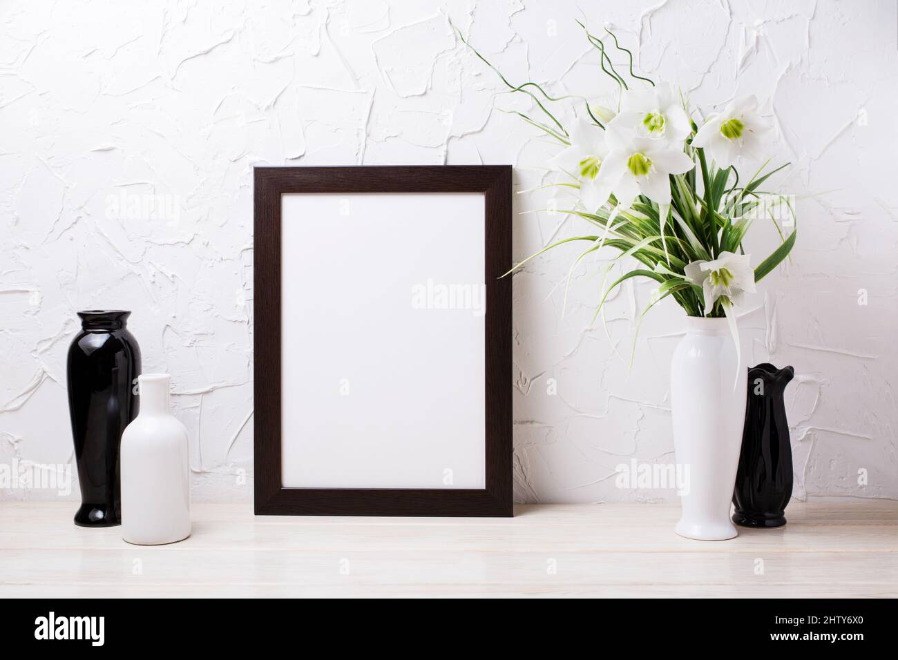 Dark brown  frame mockup with tender lily bouquet, white and black vases. Empty frame mock up for presentation design. Template framing for modern art Stock Photo