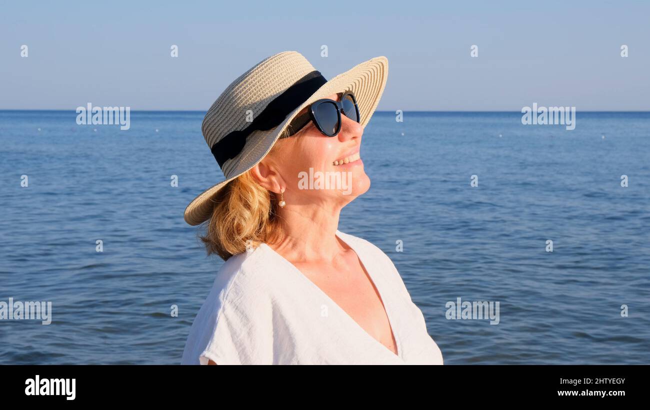 Portrait of a mature woman, age 50, wearing a straw hat and sunglasses ...