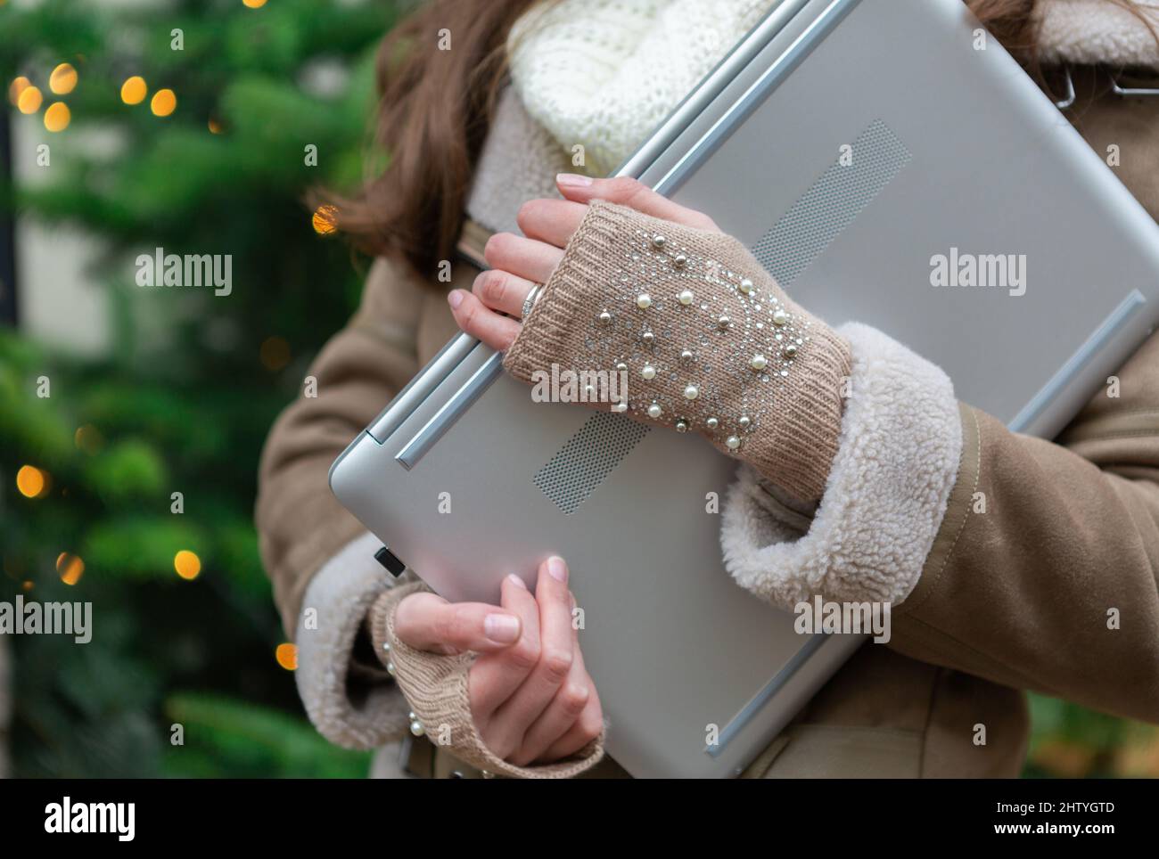 Young woman is holding her laptop with a christmas tree on the background Stock Photo