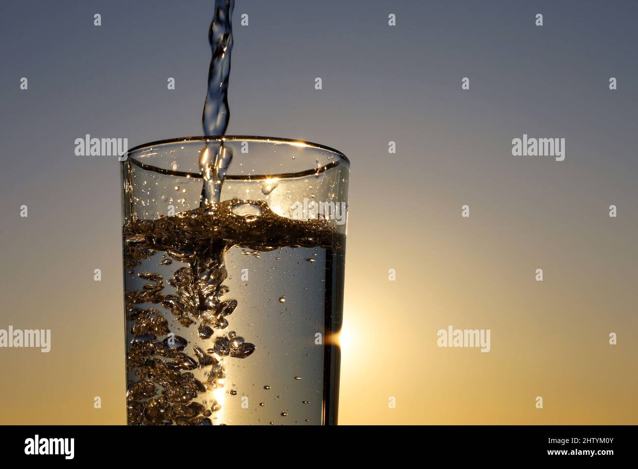 https://c8.alamy.com/comp/2HTYM0Y/clean-water-pouring-into-drinking-glass-on-sunset-sky-background-concept-of-health-and-freshness-thirst-water-purification-2HTYM0Y.jpg
