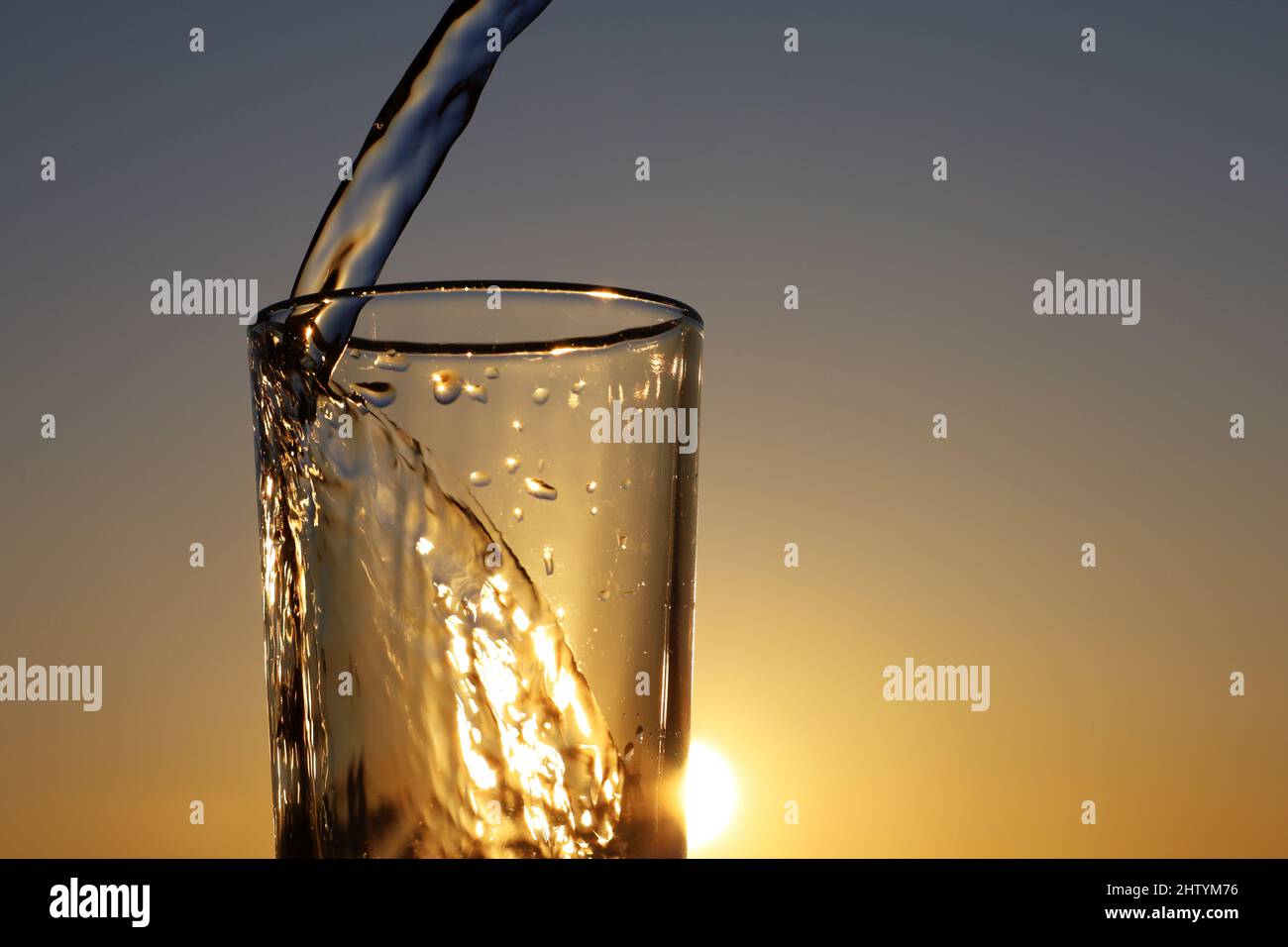 https://c8.alamy.com/comp/2HTYM76/clean-water-pouring-into-drinking-glass-on-sunset-sky-background-concept-of-health-and-freshness-thirst-water-purification-2HTYM76.jpg