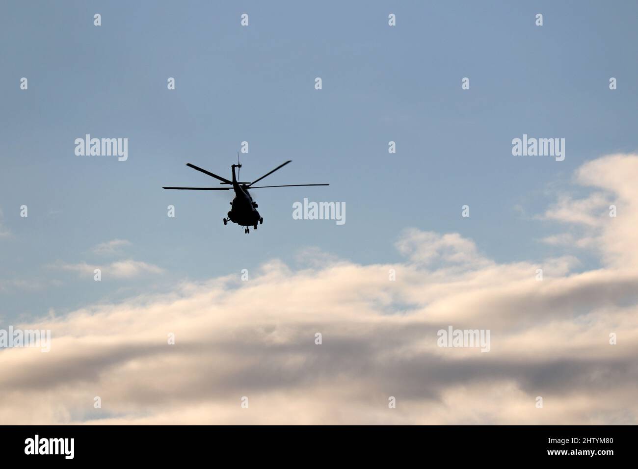 Silhouette of military helicopter in flight in blue sky with clouds Stock Photo