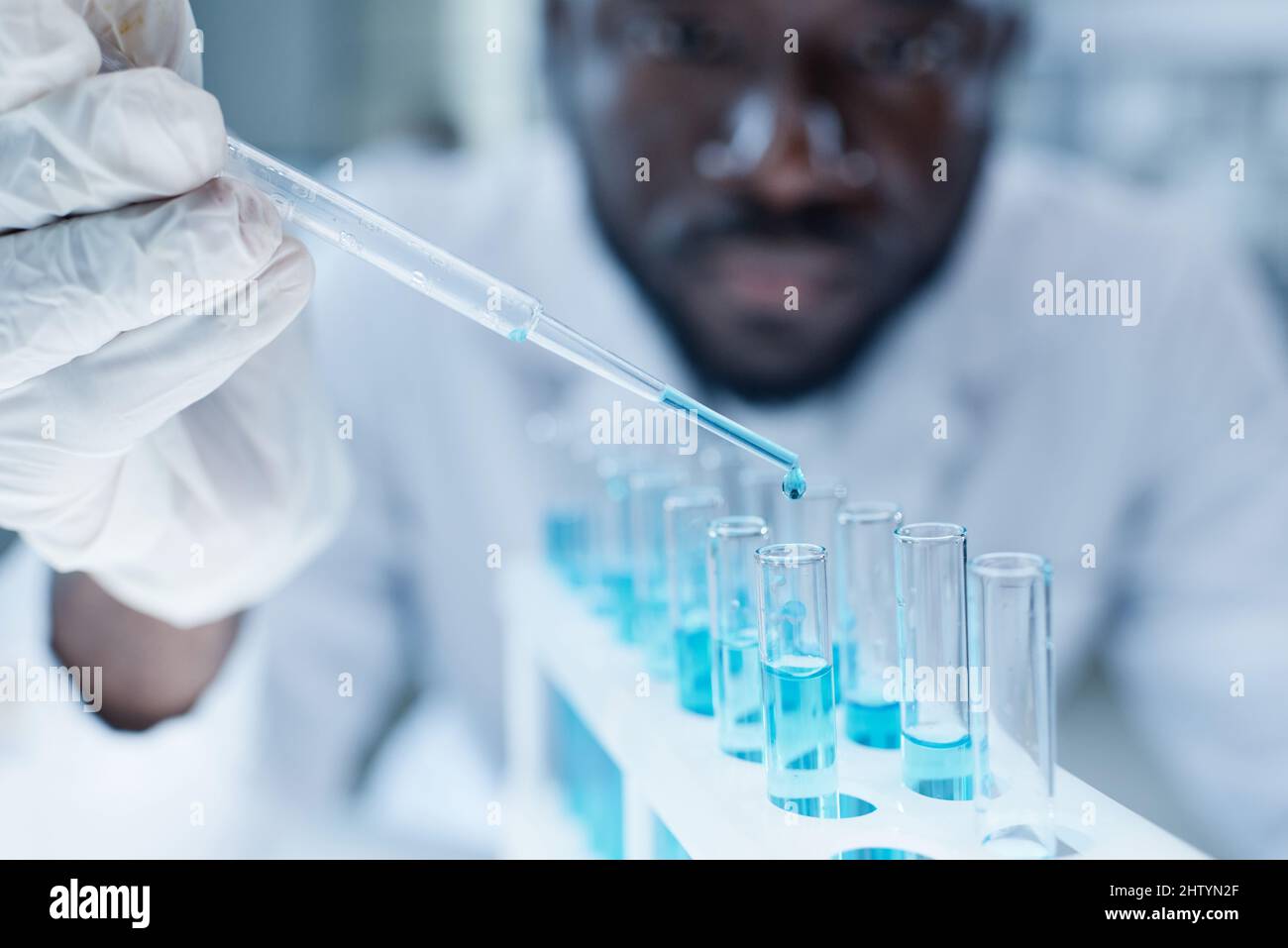 African scientist adding blue liquid with pipette into flask while examining samples in laboratory Stock Photo