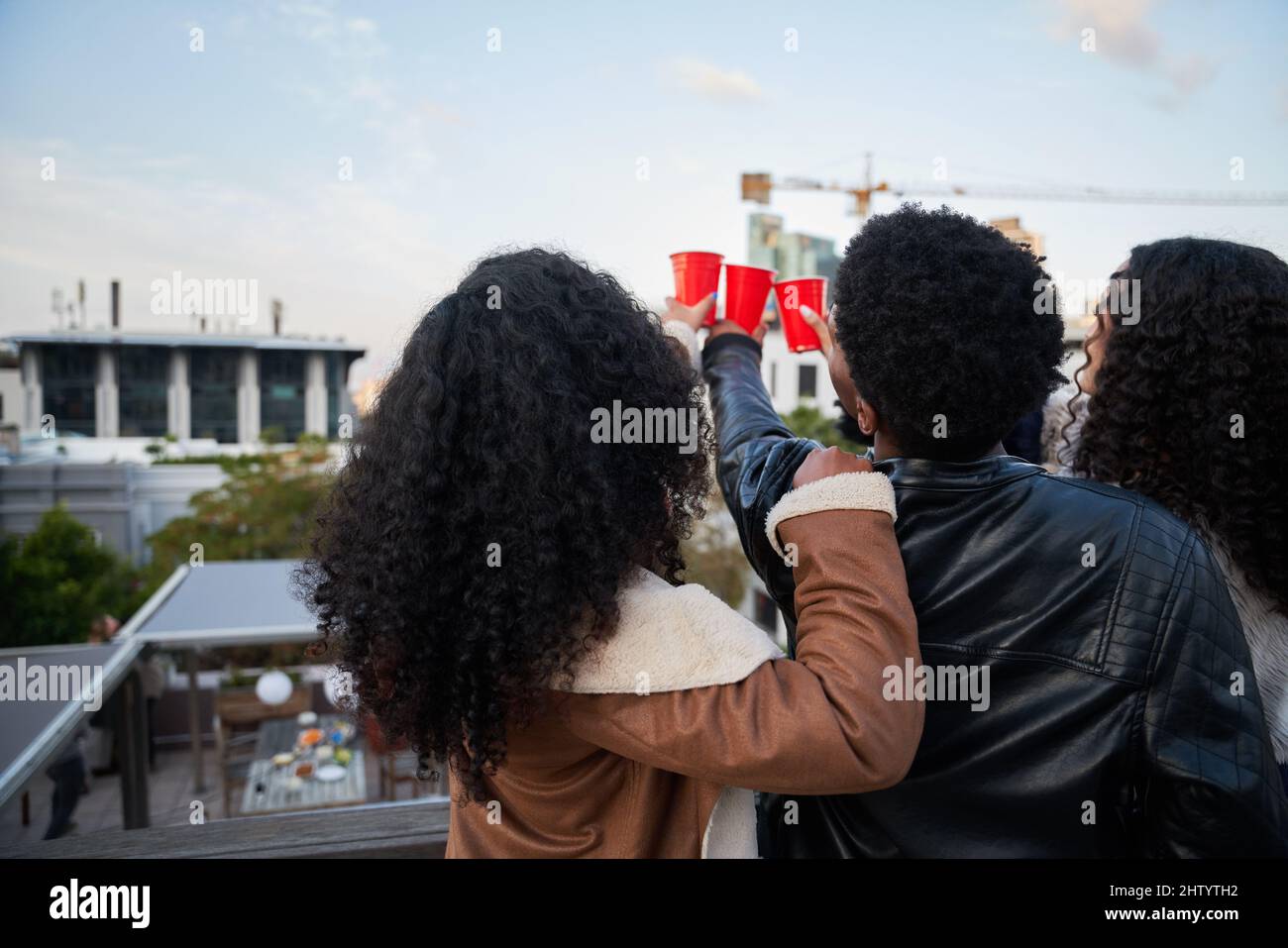 Group of multi-cultural young adults on a rooftop terrace making a toast socializing, looking at view. Stock Photo