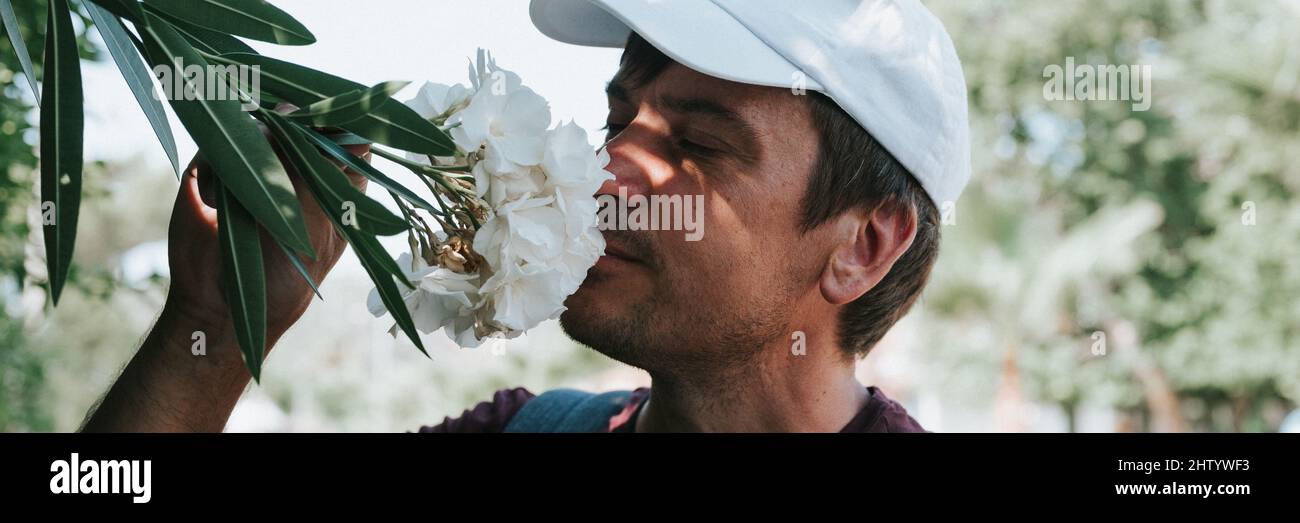 mature real candid man traveler enjoys the scent of a flowers in hand holding on a summer journey everyday moment. concept of stereotypes-free positiv Stock Photo