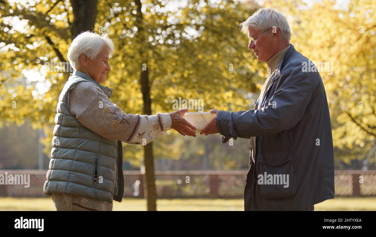 Caucasian elderly volunteers giving food to poor people in desperate need. Outdoors. High quality photo Stock Photo