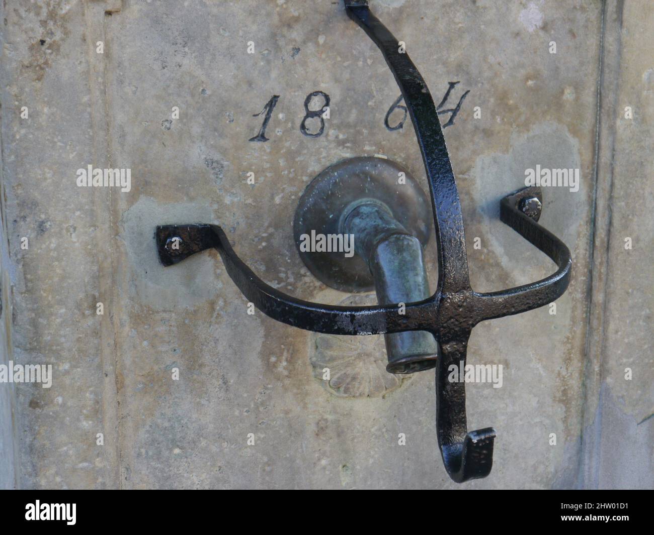 Black wrought iron protective grille on the tap of a well. Bronze water fitting in blurred background. Numbers indicate the year of construction 1864. Stock Photo