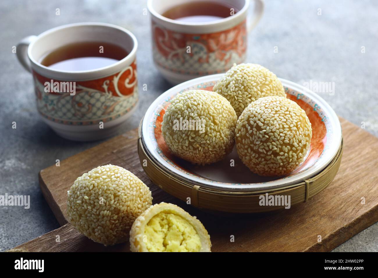 Onde Onde or glutinous rice cake sesame ball on ceramic plate with cups tea. Selective focus, grey grainy background. Stock Photo