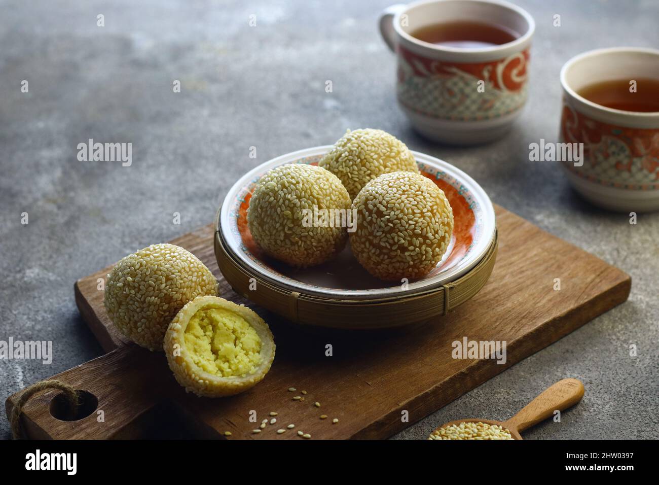Onde Onde or glutinous rice cake sesame ball on ceramic plate with cups tea. Selective focus, grey grainy background. Stock Photo