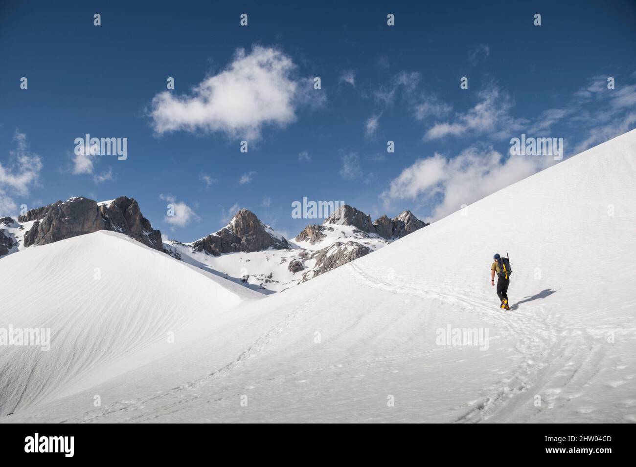 Hiker walks in the middle of a snow slope in snowy landscape in a sunny day Stock Photo