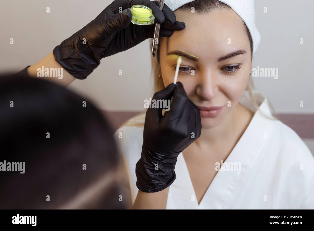 The hand of a makeup artist in black gloves applies a yellow eyebrow