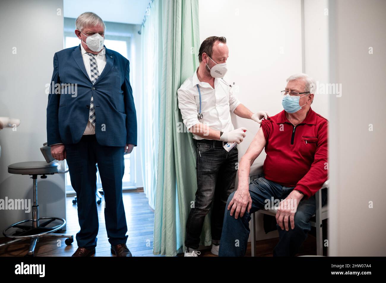 Krefeld, Germany. 03rd Mar, 2022. Physician Christian Einfalt (m) and Karl-Josef Laumann (CDU), Minister of Health of North Rhine-Westphalia, stand in the rooms of Einfalt's practice and talk to Rüdiger Bauer (r), who is getting vaccinated. The minister visited the family doctor's practice to get a picture of the vaccination process and the day-to-day work. Credit: Fabian Strauch/dpa/Alamy Live News Stock Photo
