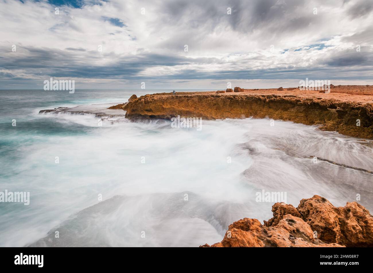 Long exposure with tourist couple on cliff face with rough waters on the rugged Indian Ocean coastline at Quobba Station in Western Australia. Stock Photo