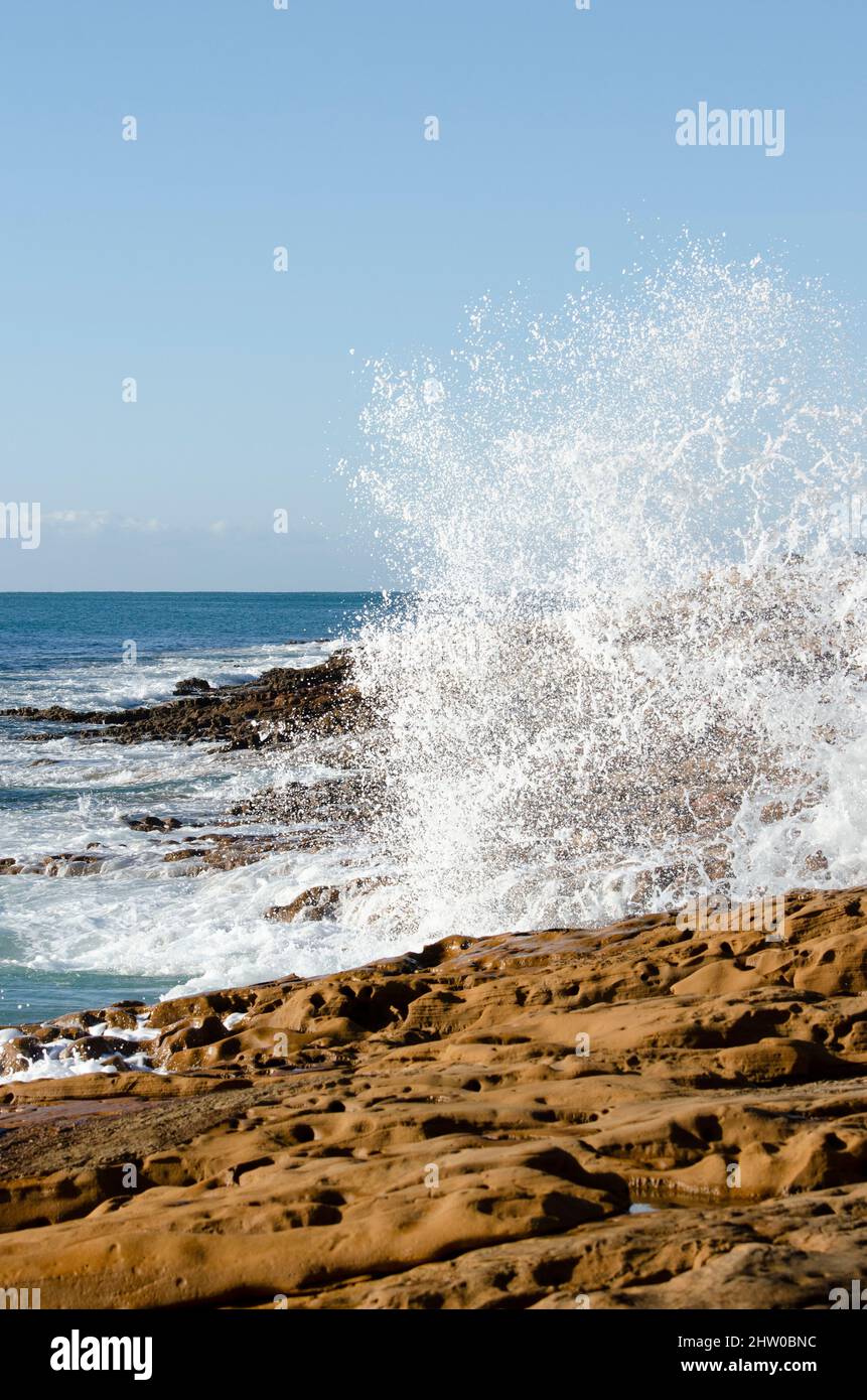 Rocky shoreline with blue sky and crashing waves Stock Photo