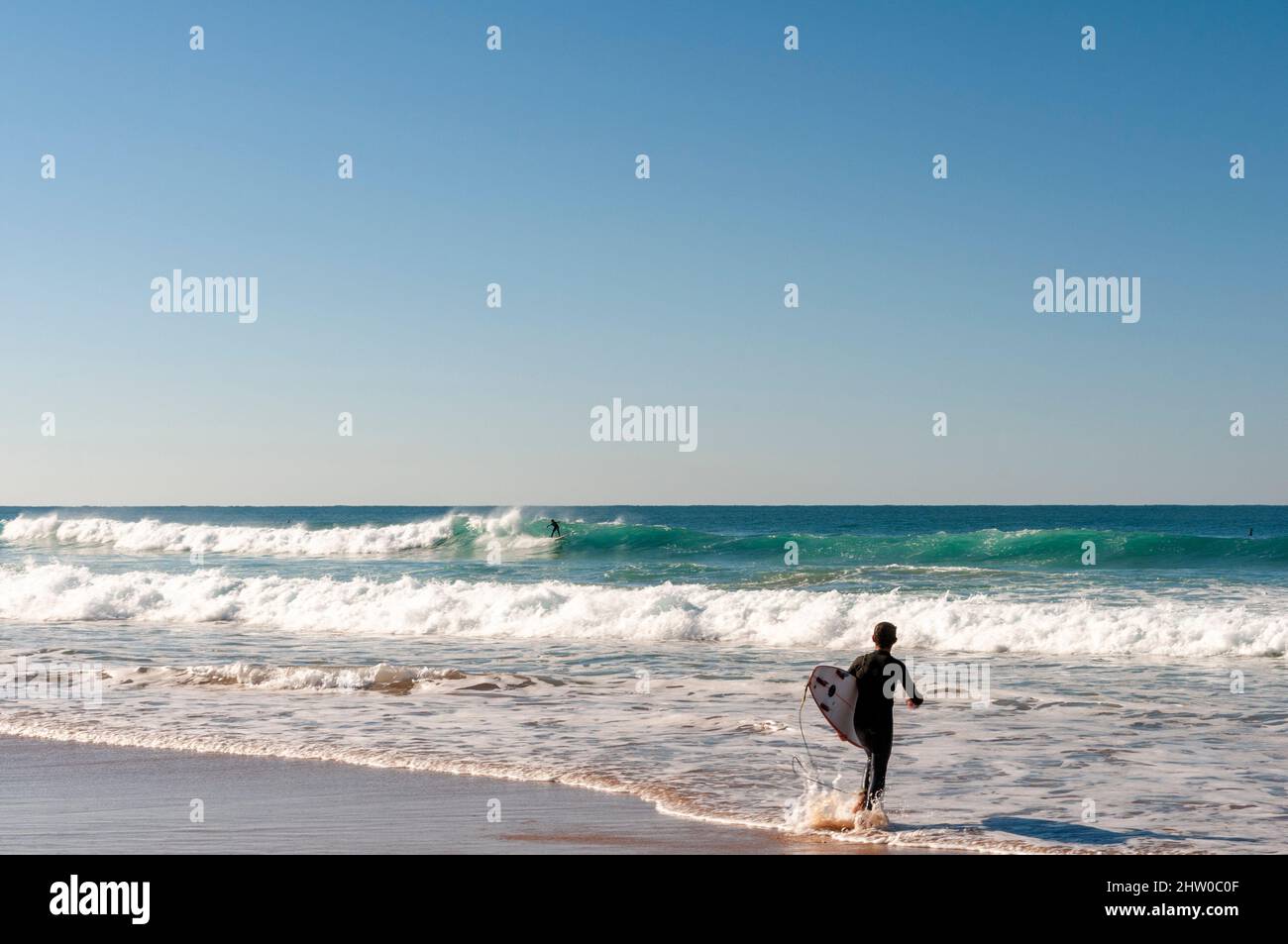Surfer entering the water with their board on beautiful Portugese beach Stock Photo