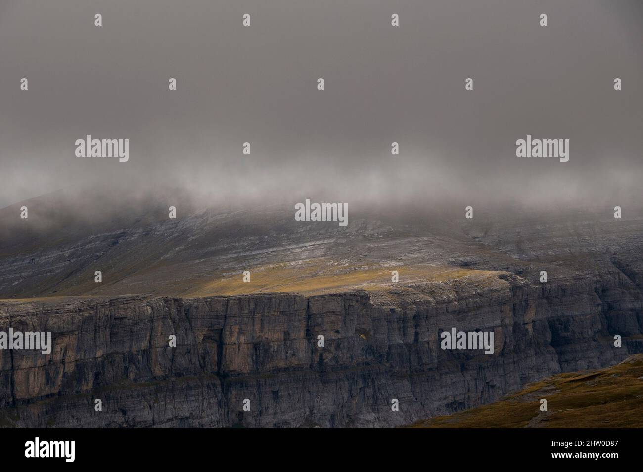 Abrupt grassy cliff slope in the mist of a dark stormy day Stock Photo