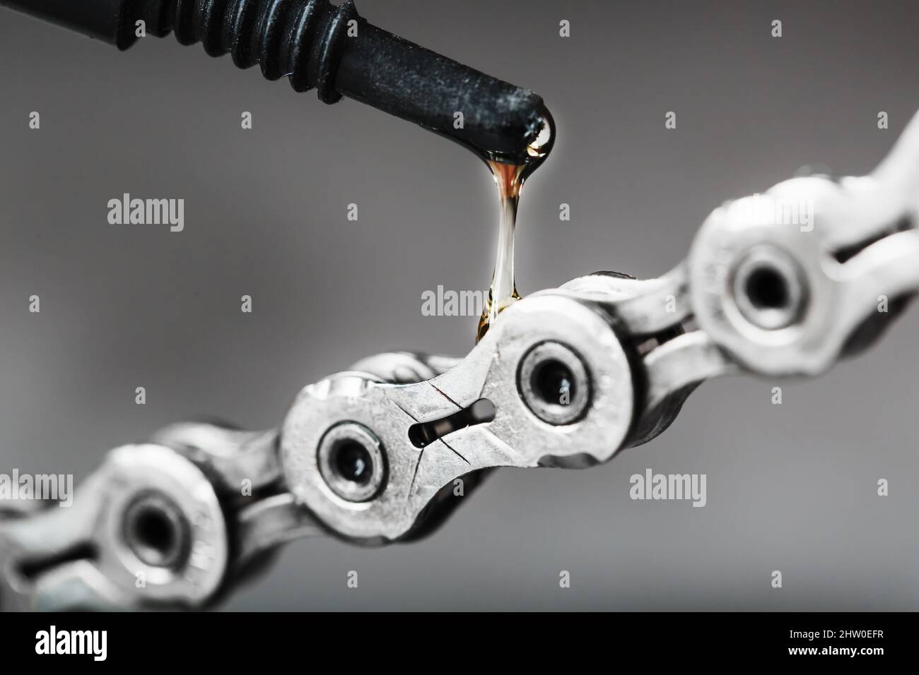 Greasing a bicycle chain with a drop of golden oil closeup on a gray