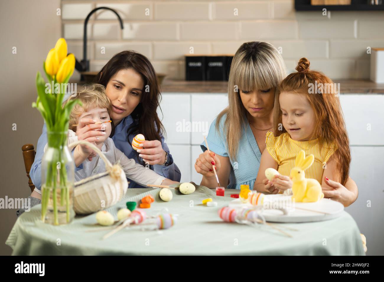 Two mothers with their children coloring Easter eggs Stock Photo