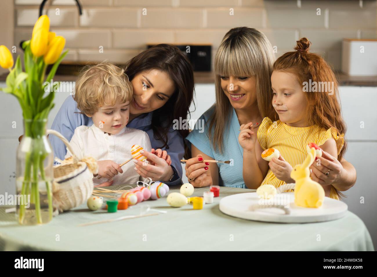Two mothers help their children paint Easter eggs Stock Photo