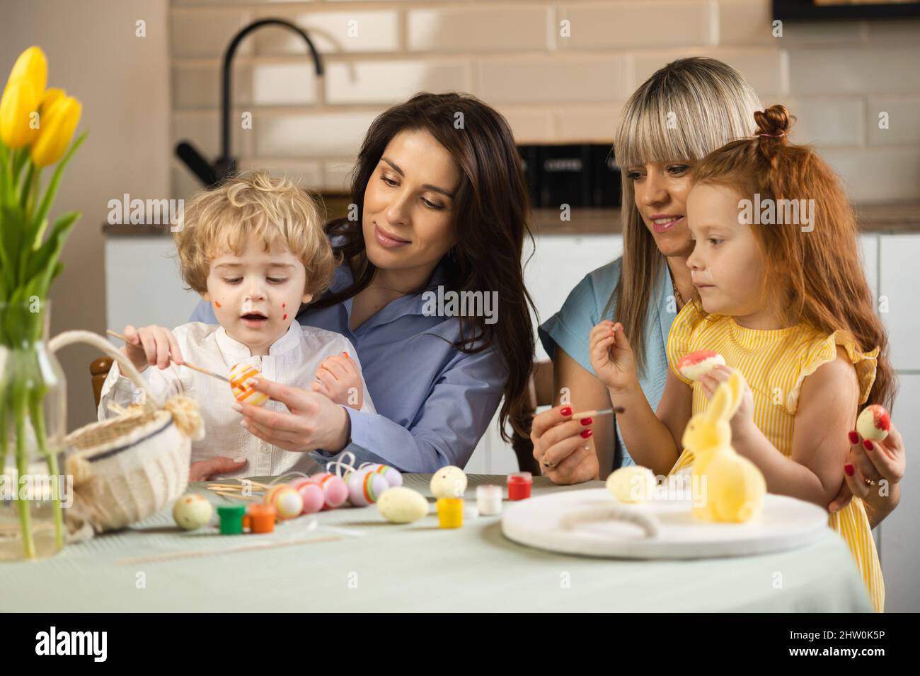 Two mothers and their children paint Easter eggs Stock Photo