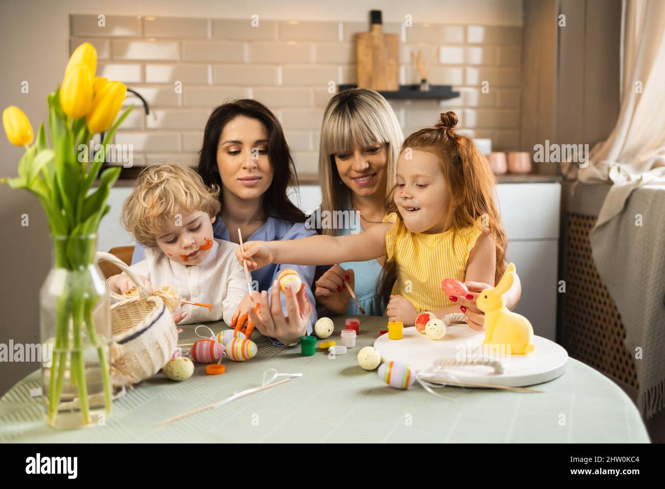 Two mothers with their children decorate Easter eggs Stock Photo