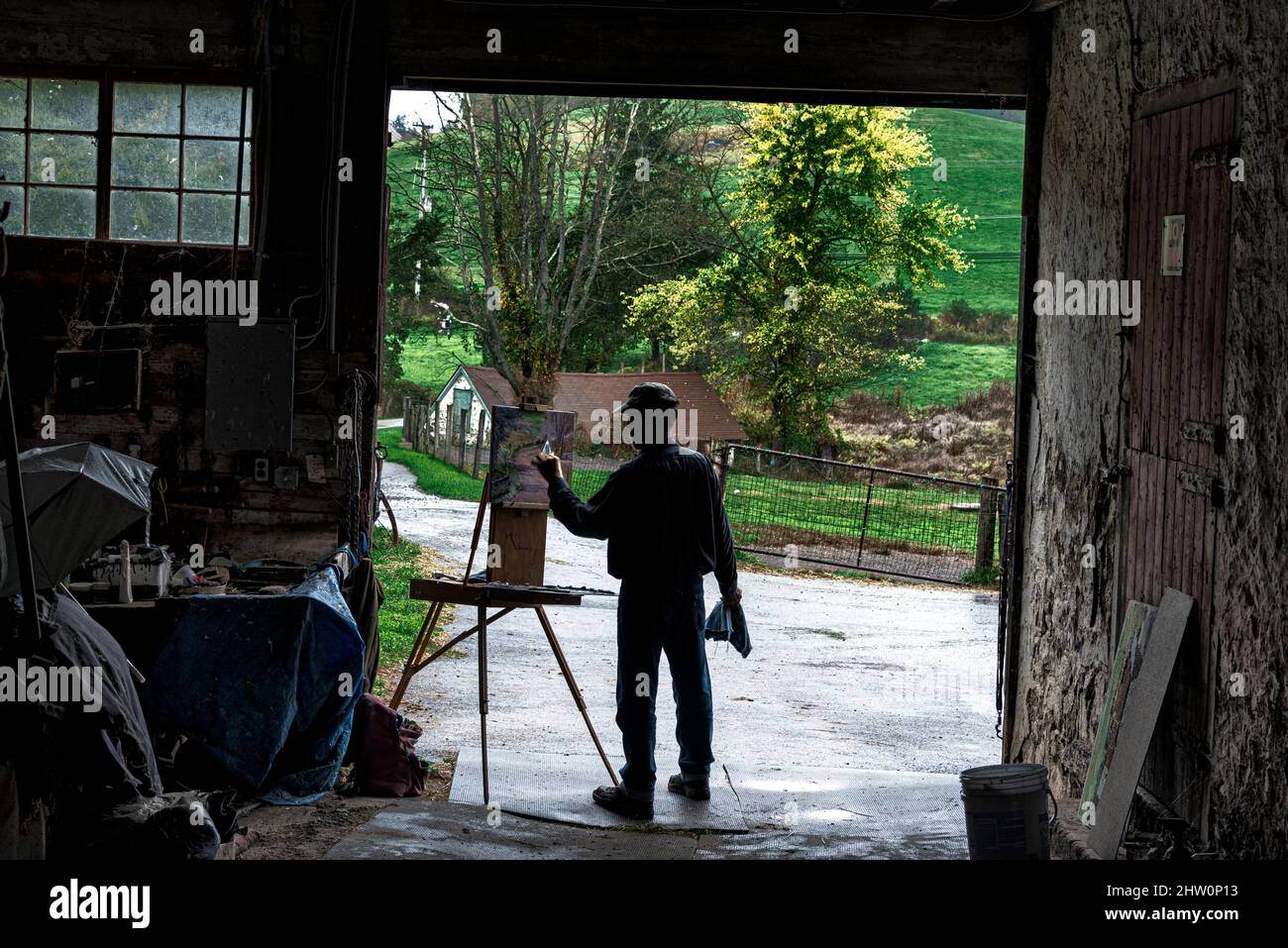 Artist paints a rural landscape from the cover of an open barn. Stock Photo