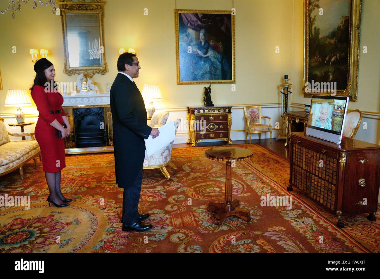 Queen Elizabeth II appears on a screen via videolink from Windsor Castle, where she is in residence, during a virtual audience to receive the High Commissioner of Trinidad and Tobago, Vishnu Dhanpaul (centre), and Mrs. Geofroy-Dhanpaul (left), at Buckingham Palace, London. Picture date: Thursday March 3, 2022. Stock Photo