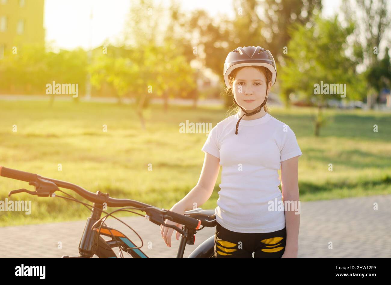 Girl with a bike in the park. An 11-year-old girl in a protective sports helmet next to a bicycle. Children's sports and a healthy lifestyle Stock Photo