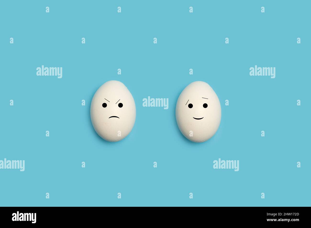 Two eggs with happy and angry face shape on a blue background Stock Photo