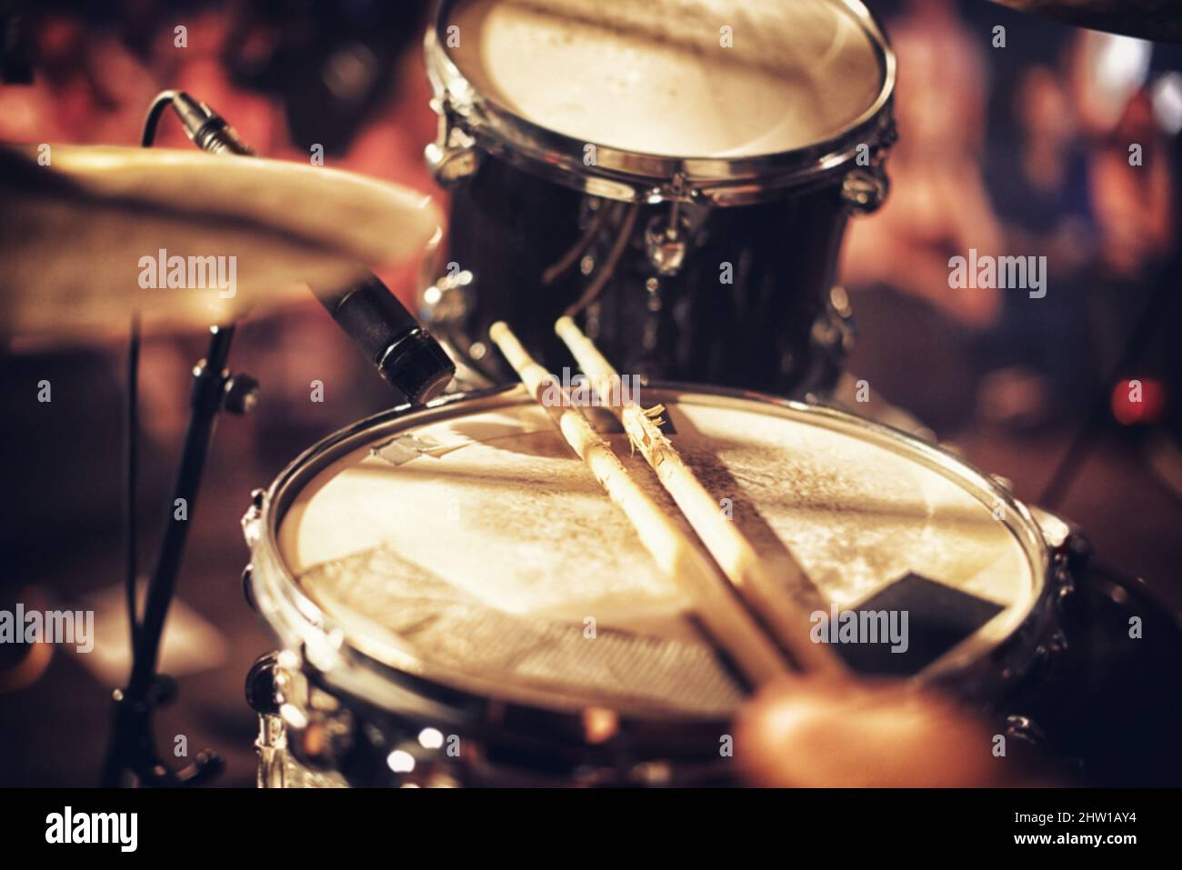 A beat waiting to happen. Drum kit set up on a stage with a crowd in the background. Stock Photo