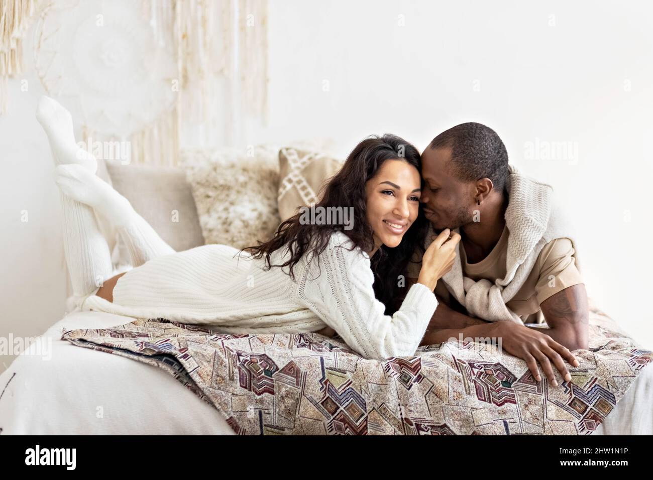 A couple in love - a black man and a mulatto woman on a bed in a bright room. Diverse family. Stock Photo