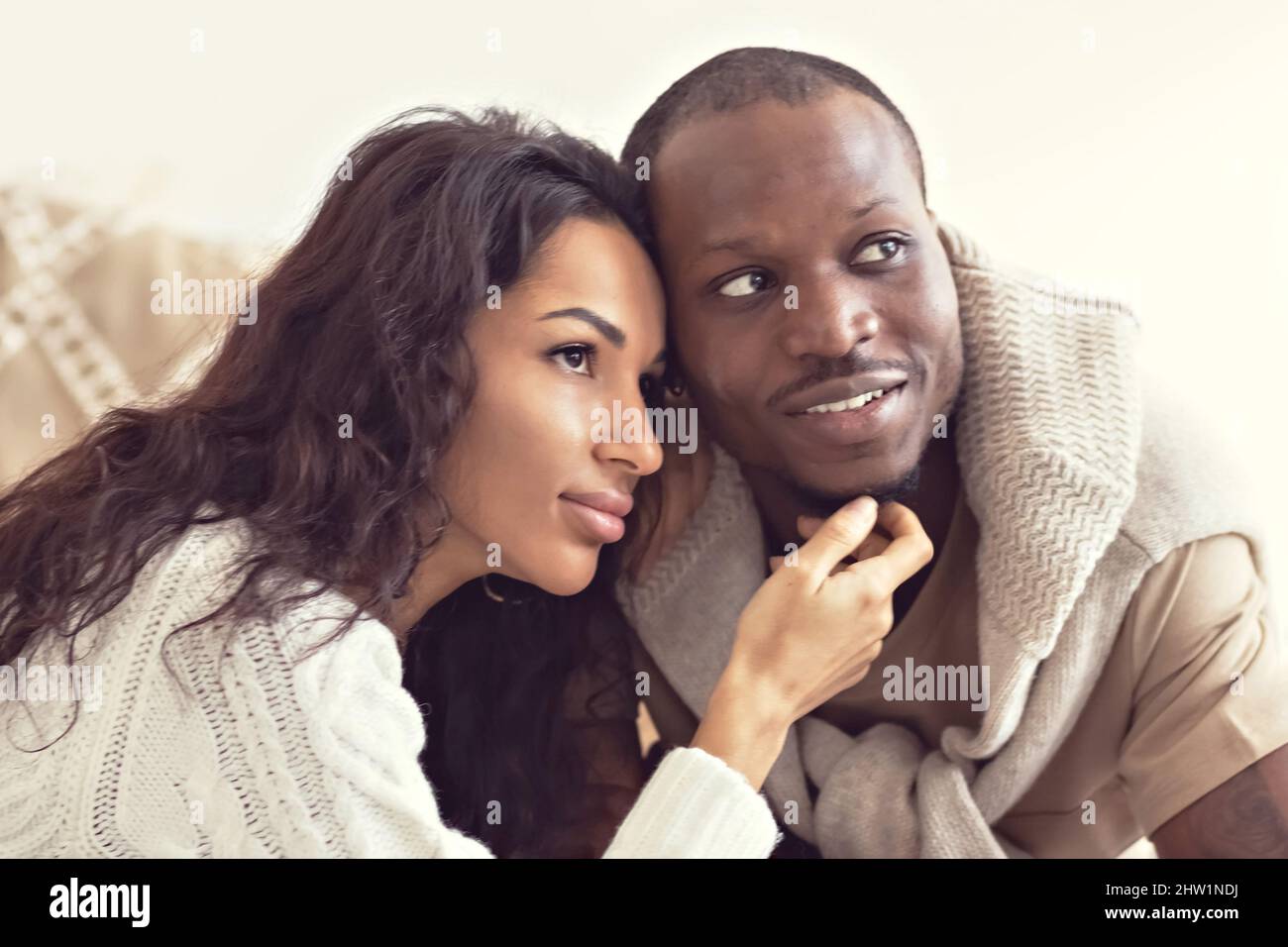 A couple in love - a black man and a mulatto woman on a bed in a bright room. Diverse family. Stock Photo