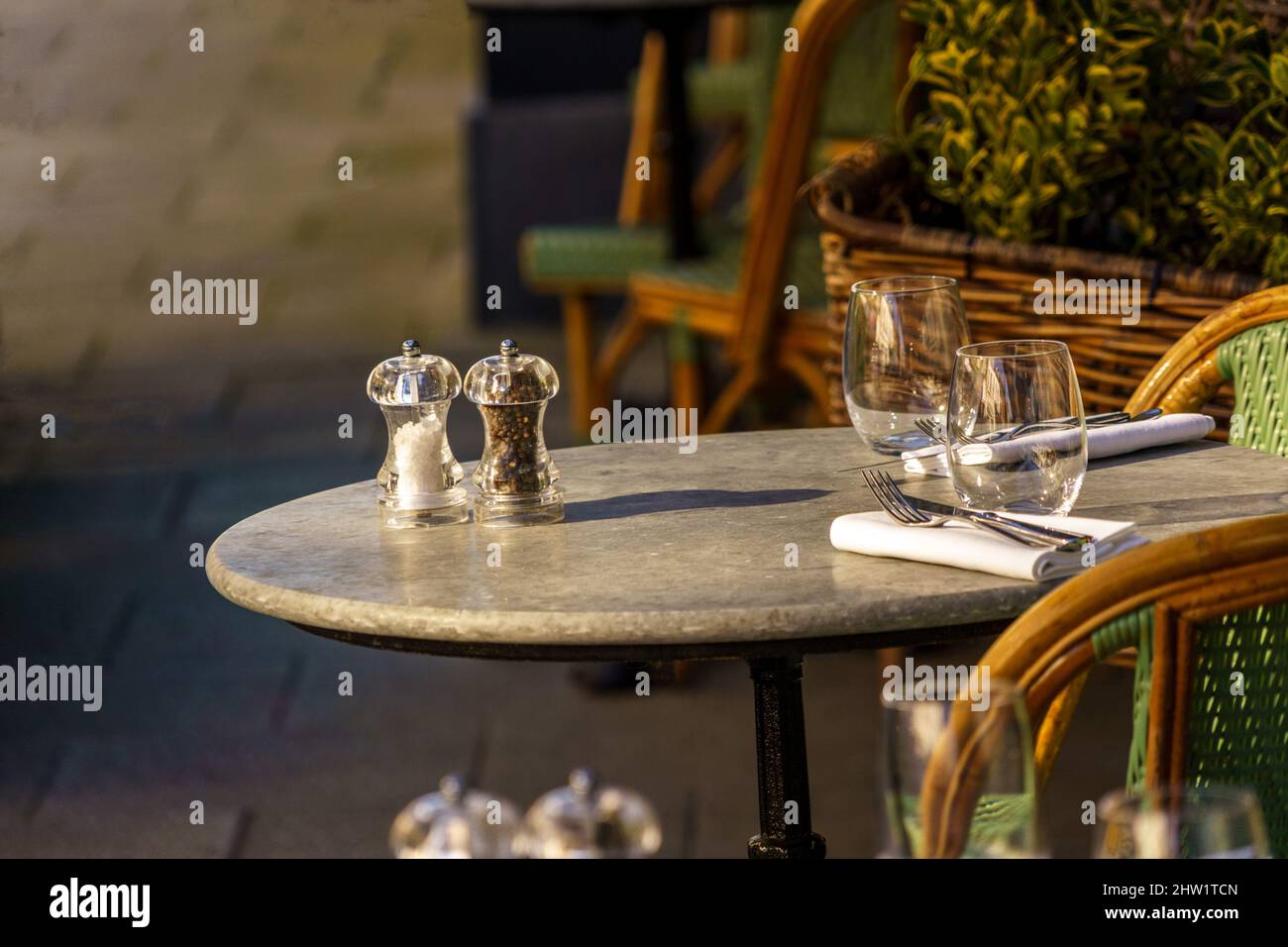 A restaurant's outdoor stemless wine glasses, napkins, cutlery, and salt and pepper grinders sit atop a circular table.. Stock Photo