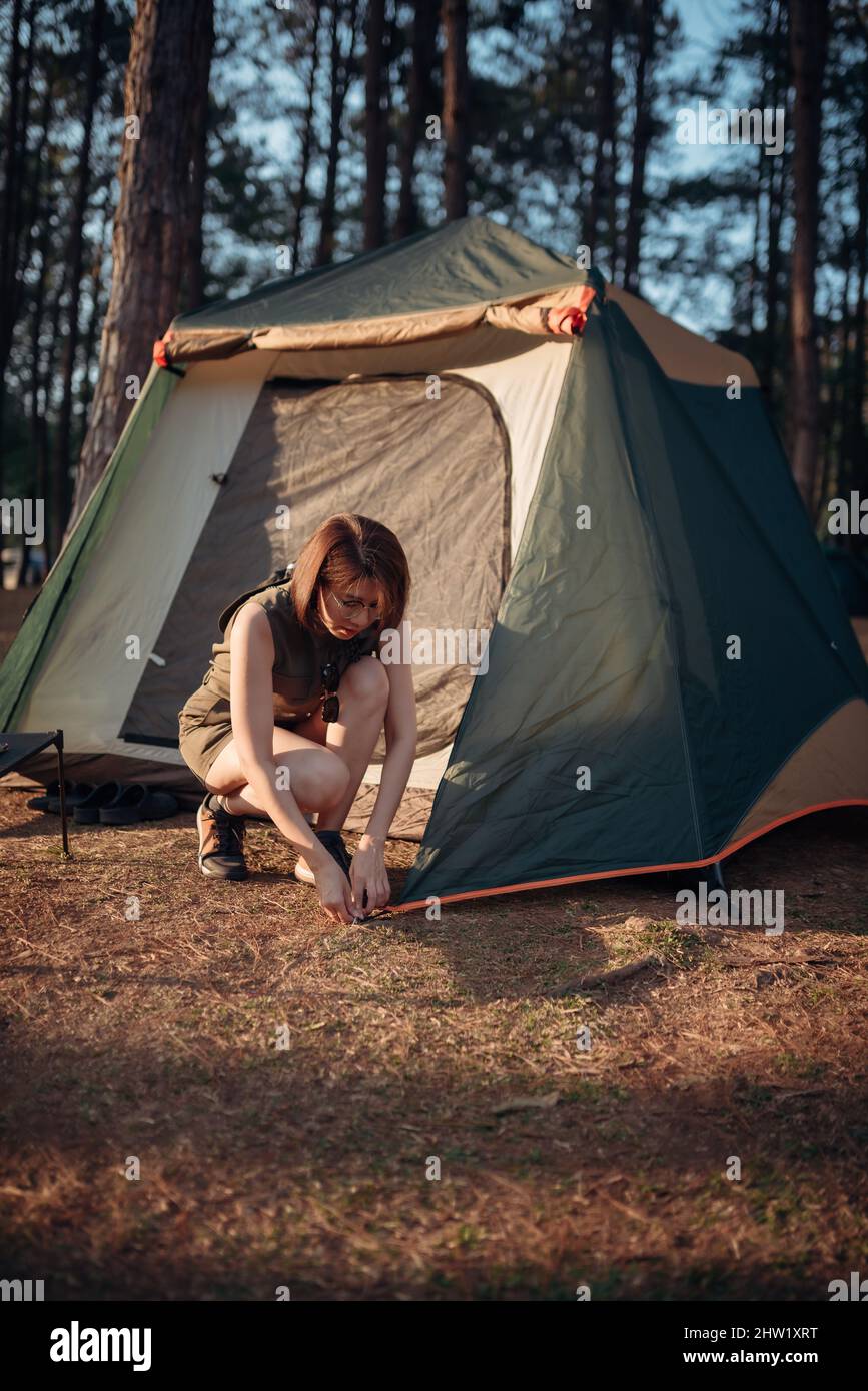 An Asian woman is pitching a tent in the pine tree forest at Pang Oung, Mae Hong Son province, Thailand. Stock Photo