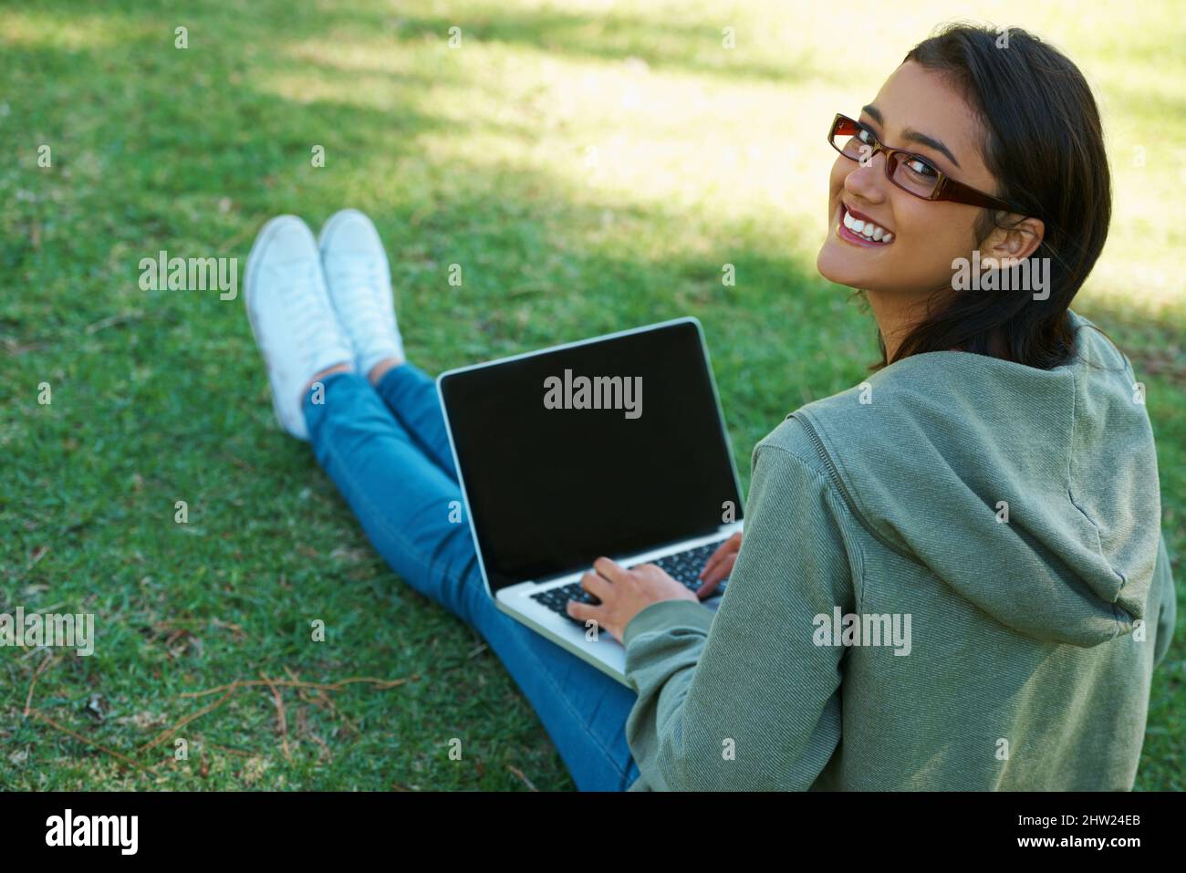 Connected - anywhere, anytime. A young woman working on her laptop in the park. Stock Photo