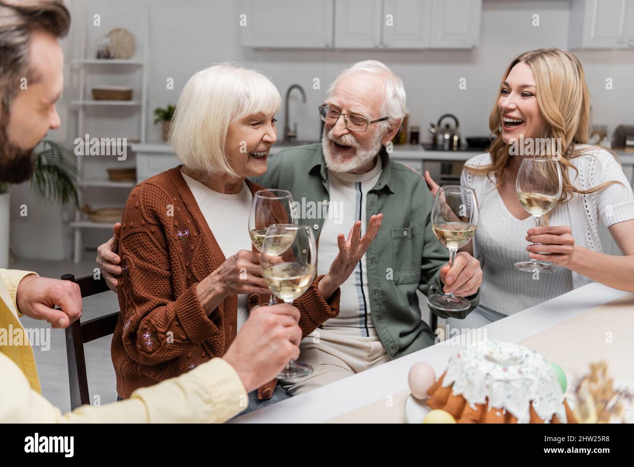 senior woman holding glass of wine and laughing during family dinner ...