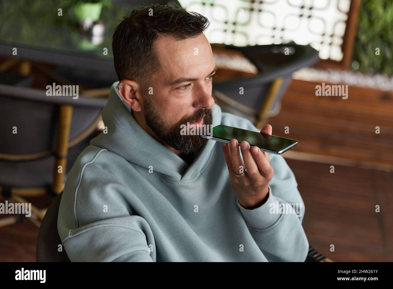 Serious young adult man in casual clothes in cafe records audio messages Stock Photo