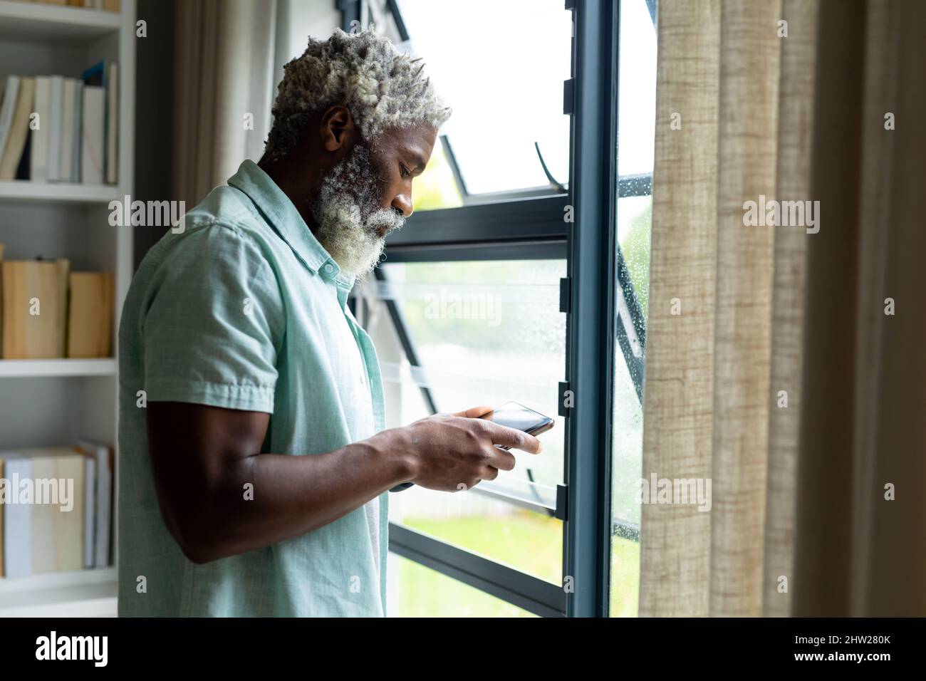 African american man using tablet pc while standing by window at home Stock Photo