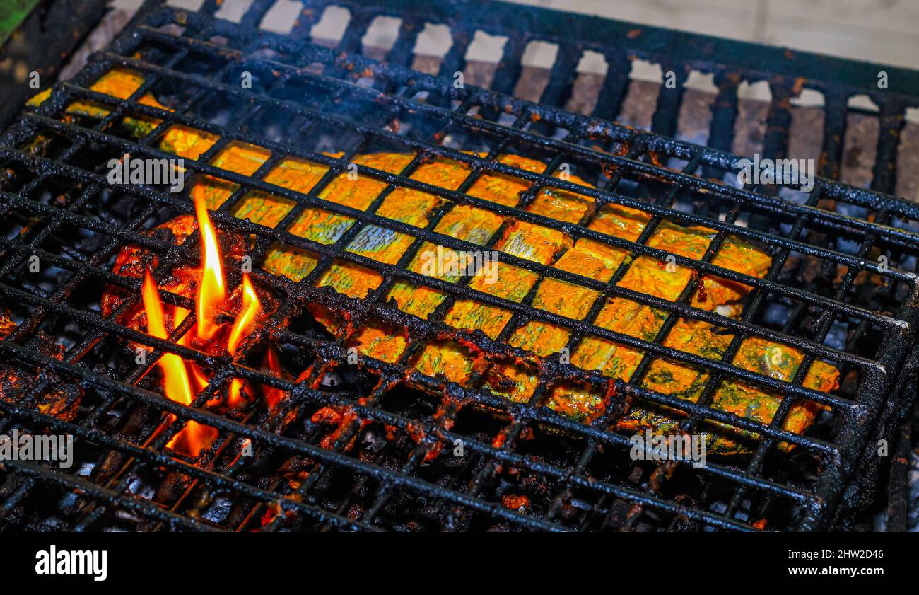 Fish on the grill, Close up of seafood grilled fish food with salt on the grill fire and smoke on dark background. fish cooked at the stake, camping l Stock Photo