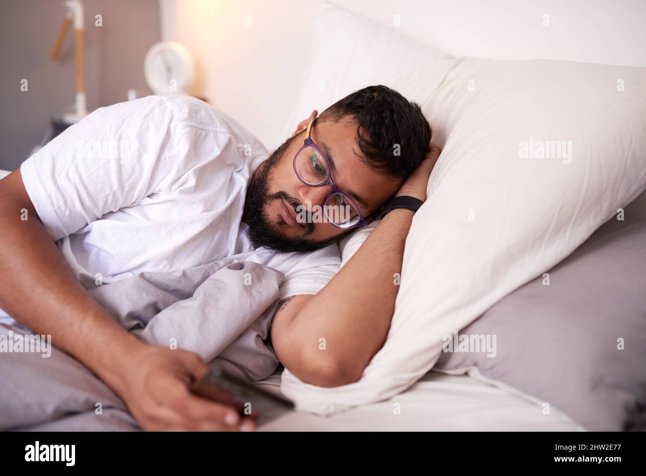 A man wearing spectacles looking at his mobile phone while lying in bed Stock Photo