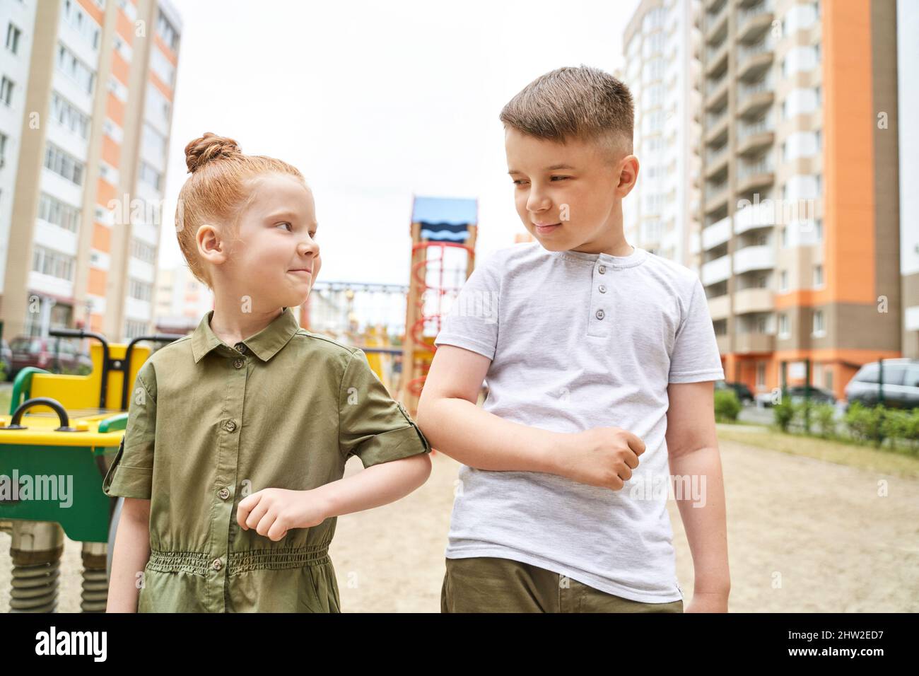 Elbow touch. New normal. Corona virus safety handshake. Boy and girl greating. Family sign. Arm salute gesture. Playground background. Outdoors. Healt Stock Photo