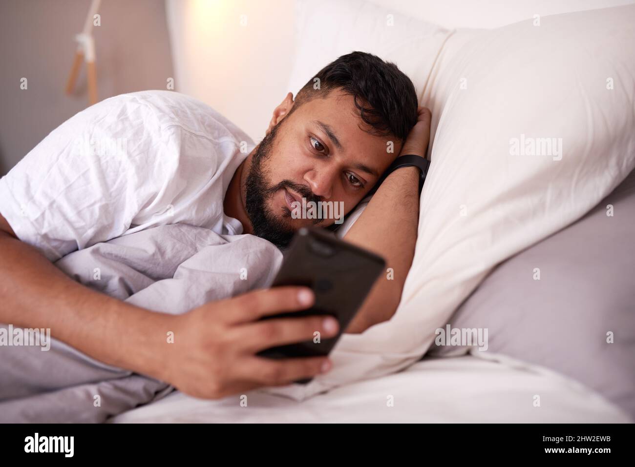 A man looking at his mobile phone while lying in bed Stock Photo