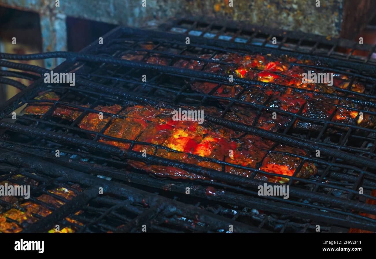 Fish on the grill, Close up of seafood grilled fish food with salt on the grill fire and smoke on dark background. fish cooked at the stake, camping l Stock Photo